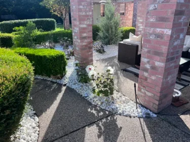 Gravel pathways with river rock borders, manicured hedges, and ornamental plantings around brick structures