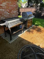 Built-in outdoor grill station with concrete pad, storage cabinets, and brick fence backdrop
